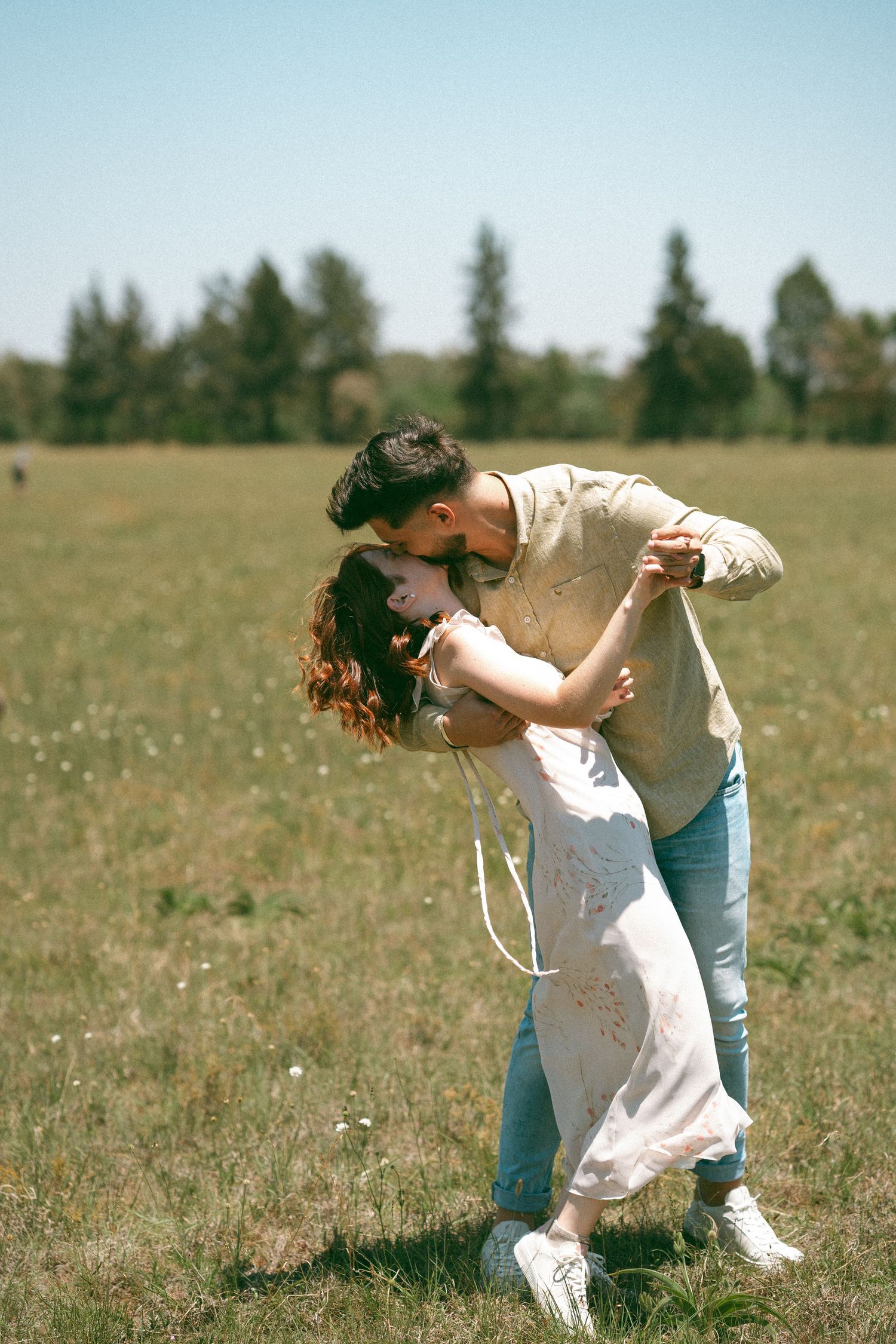 Dancing couple performs graceful movements together in an open field with trees in the background.