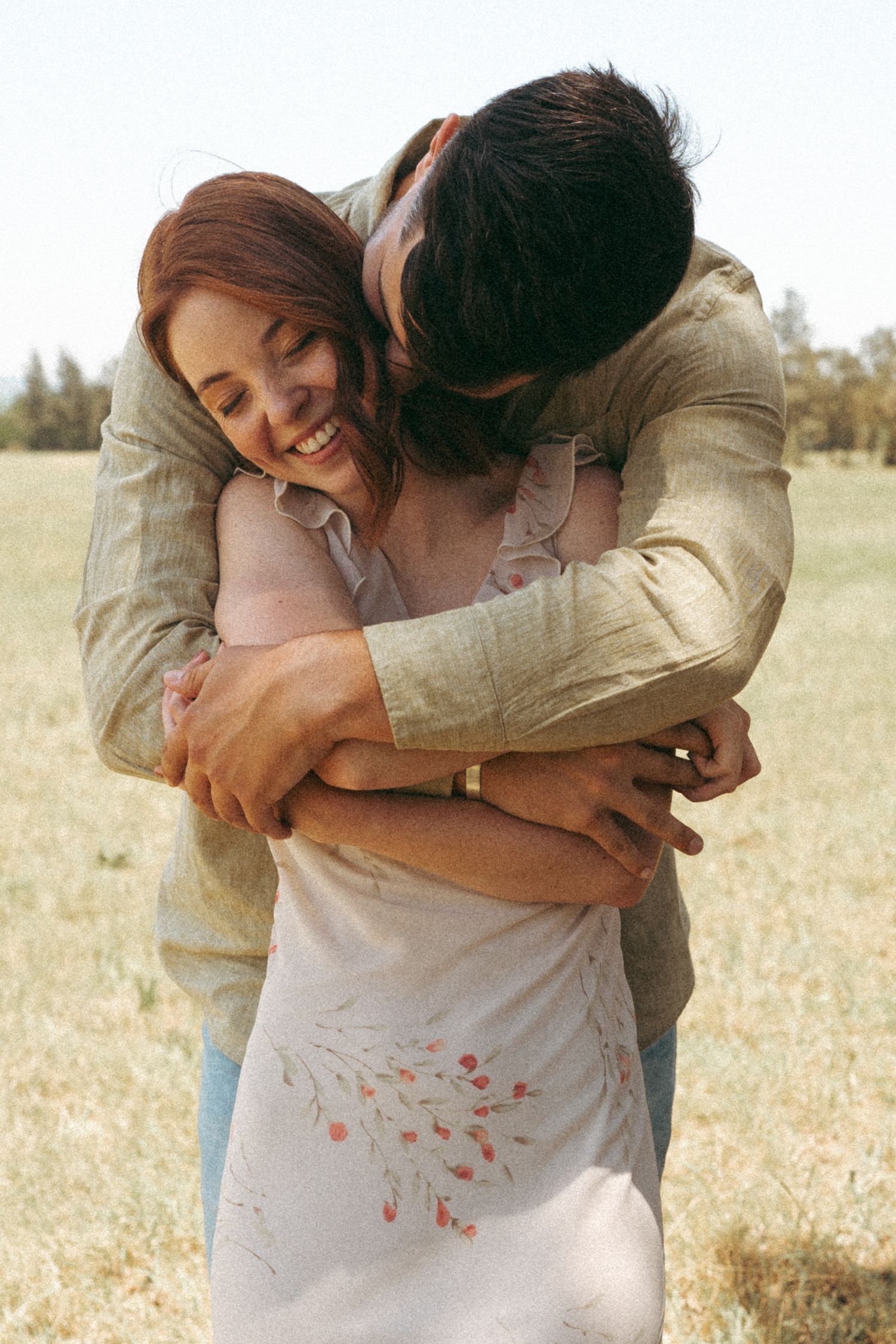 Romantic embrace captured in warm sunlight against a natural landscape.
