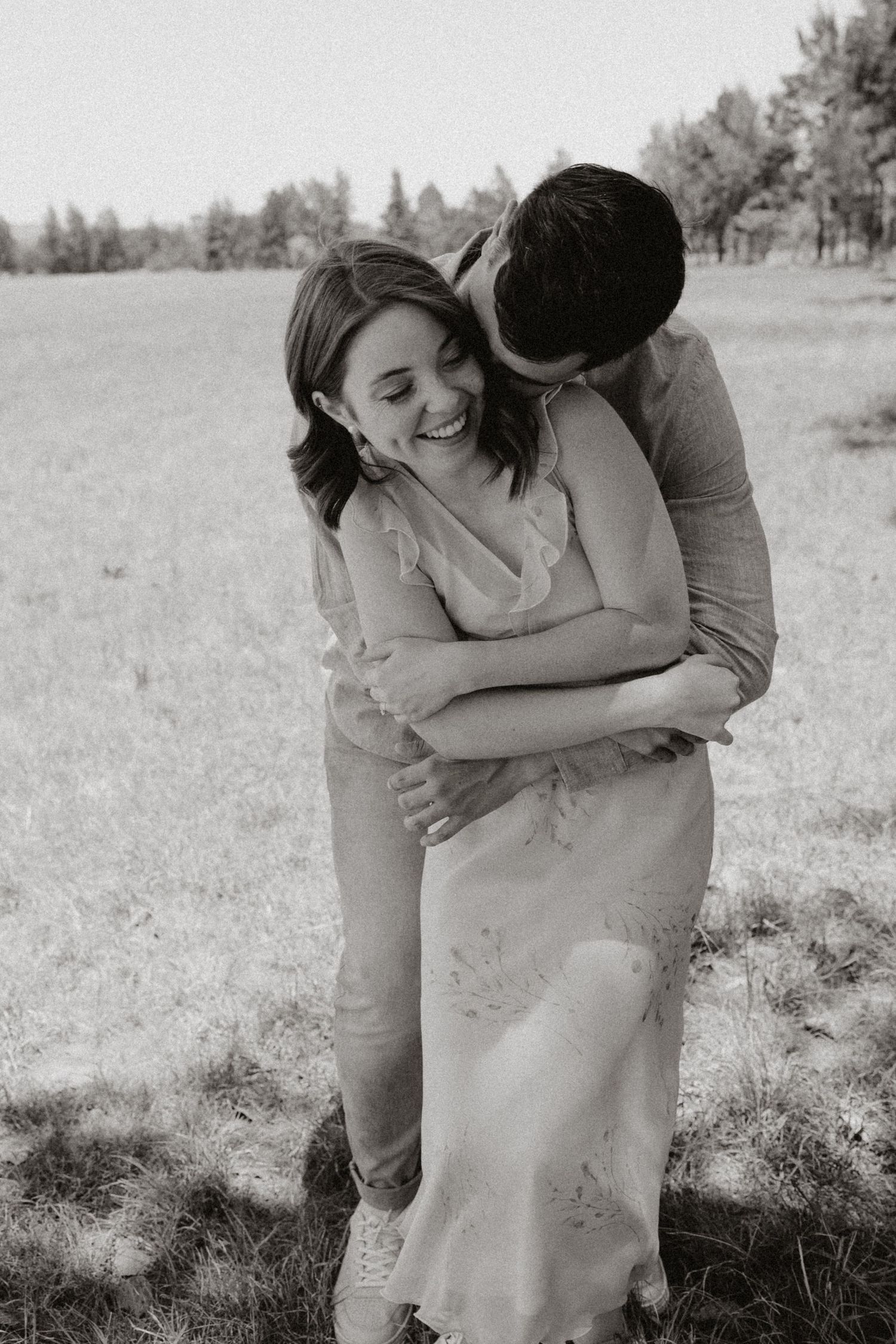 Black and white photo of a couple sharing an intimate moment in a meadow.