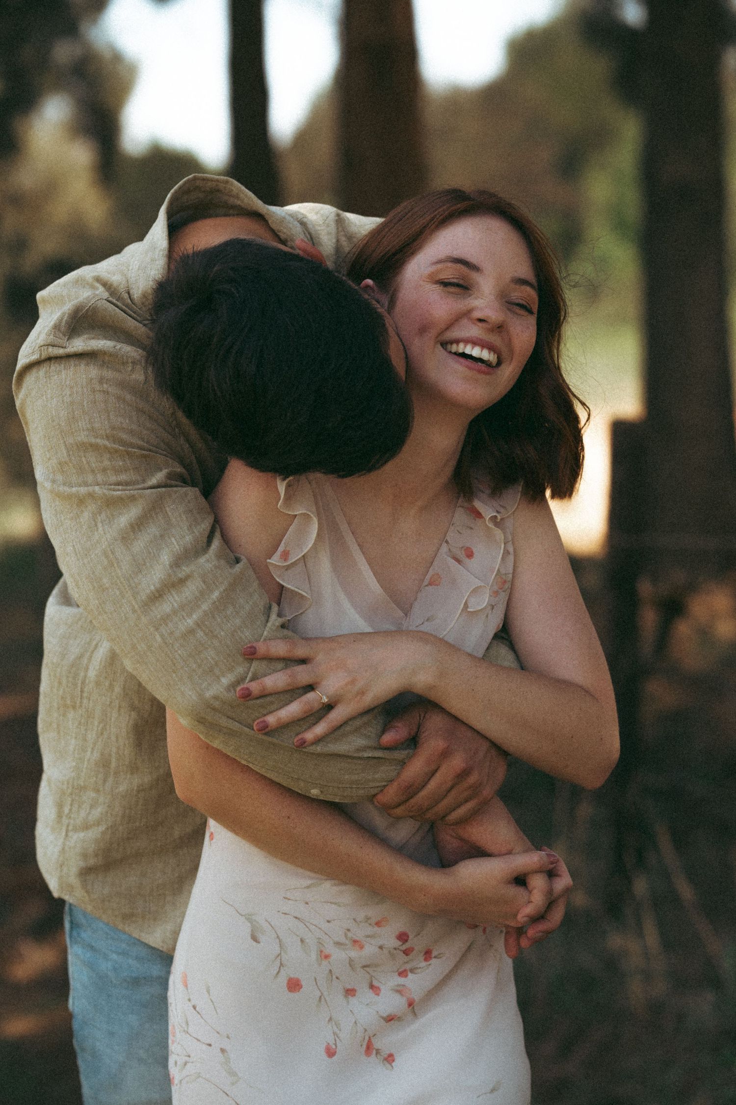 A romantic couple embraces and laughs together in a natural outdoor setting during golden hour.
