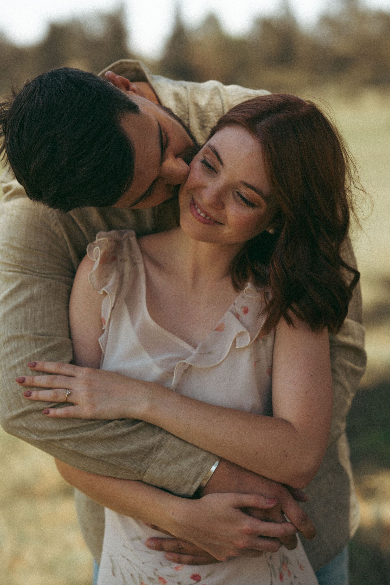 A couple shares playful embraces and laughter while posing for romantic photos outdoors.