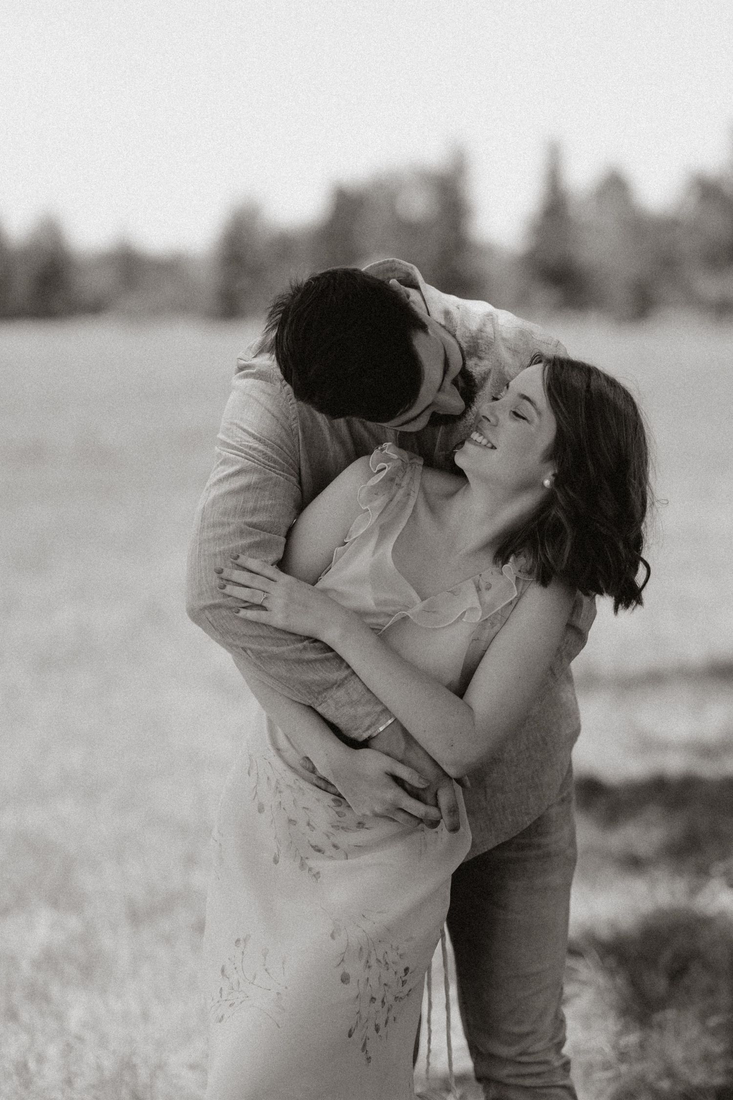 A tender black and white portrait of a couple sharing an intimate moment in a field.
