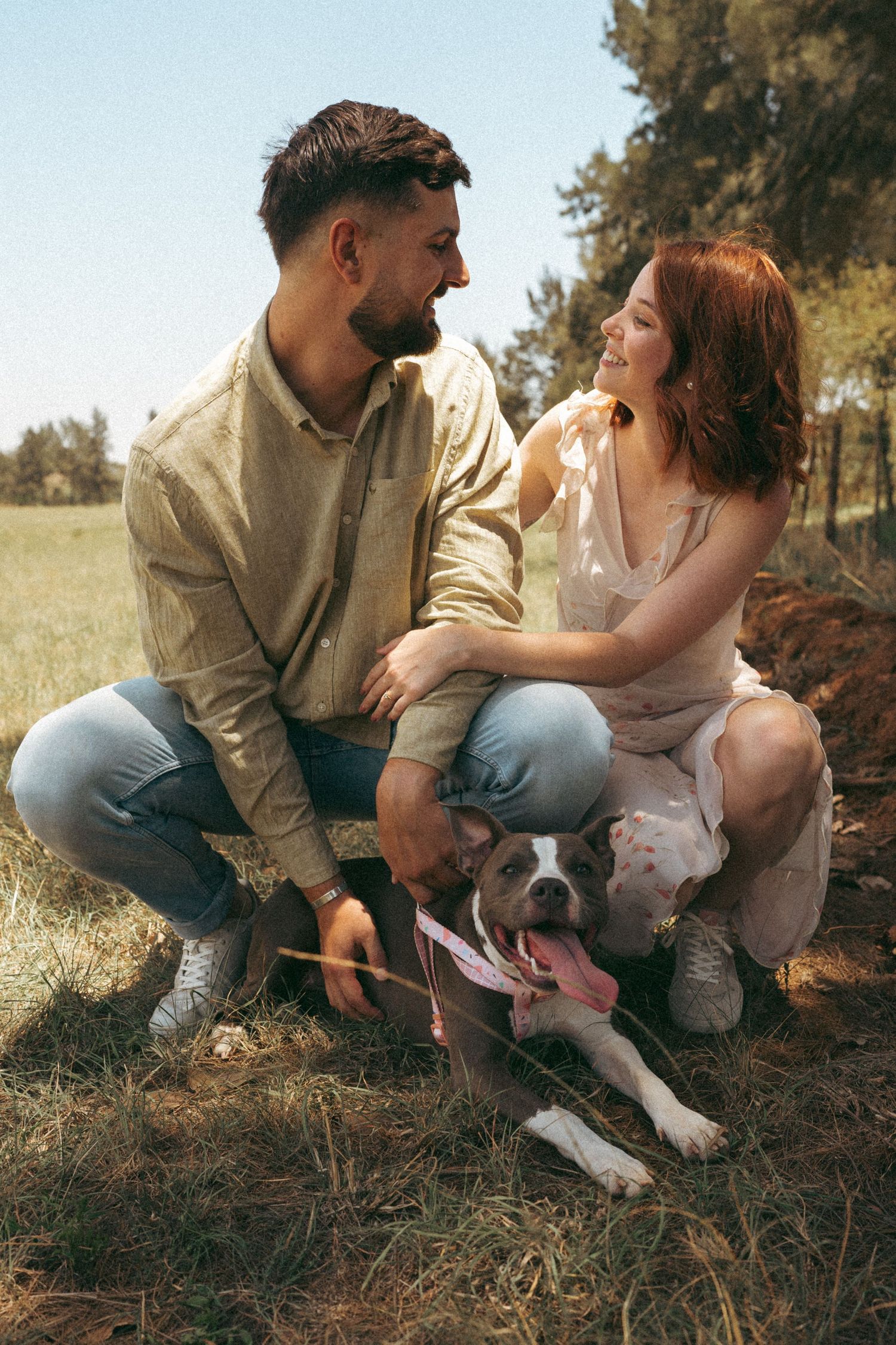 A couple sits in a grassy field with their white dog during an outdoor photoshoot.