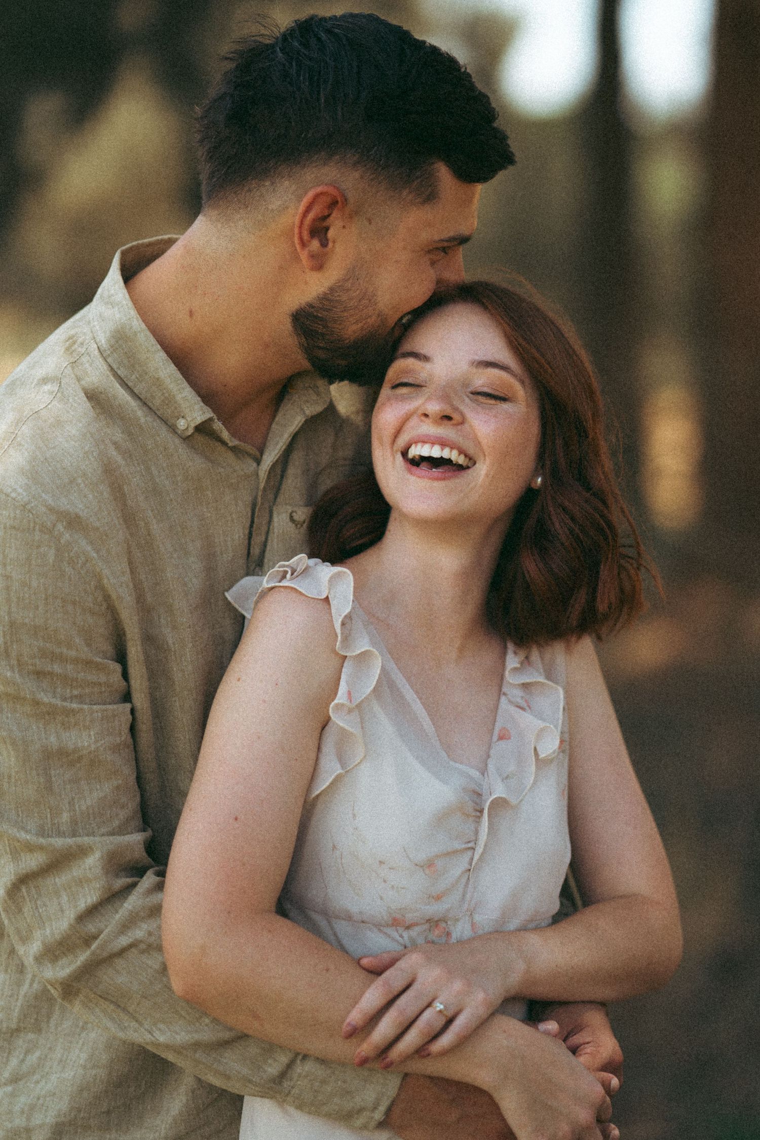 A romantic couple shares tender moments in a forest setting wearing light colored clothing.