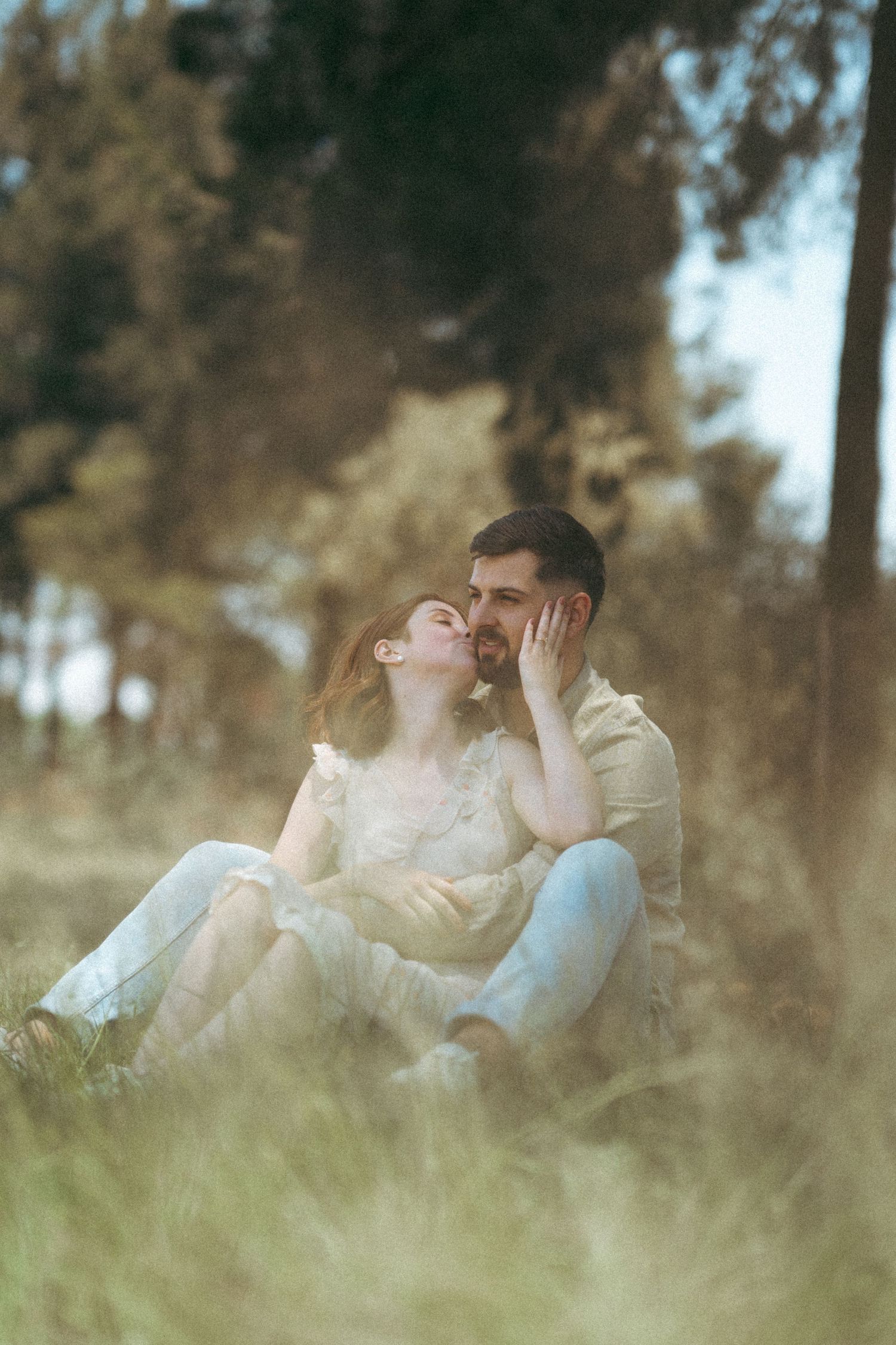 A couple lies together in tall grass during a romantic outdoor photoshoot.