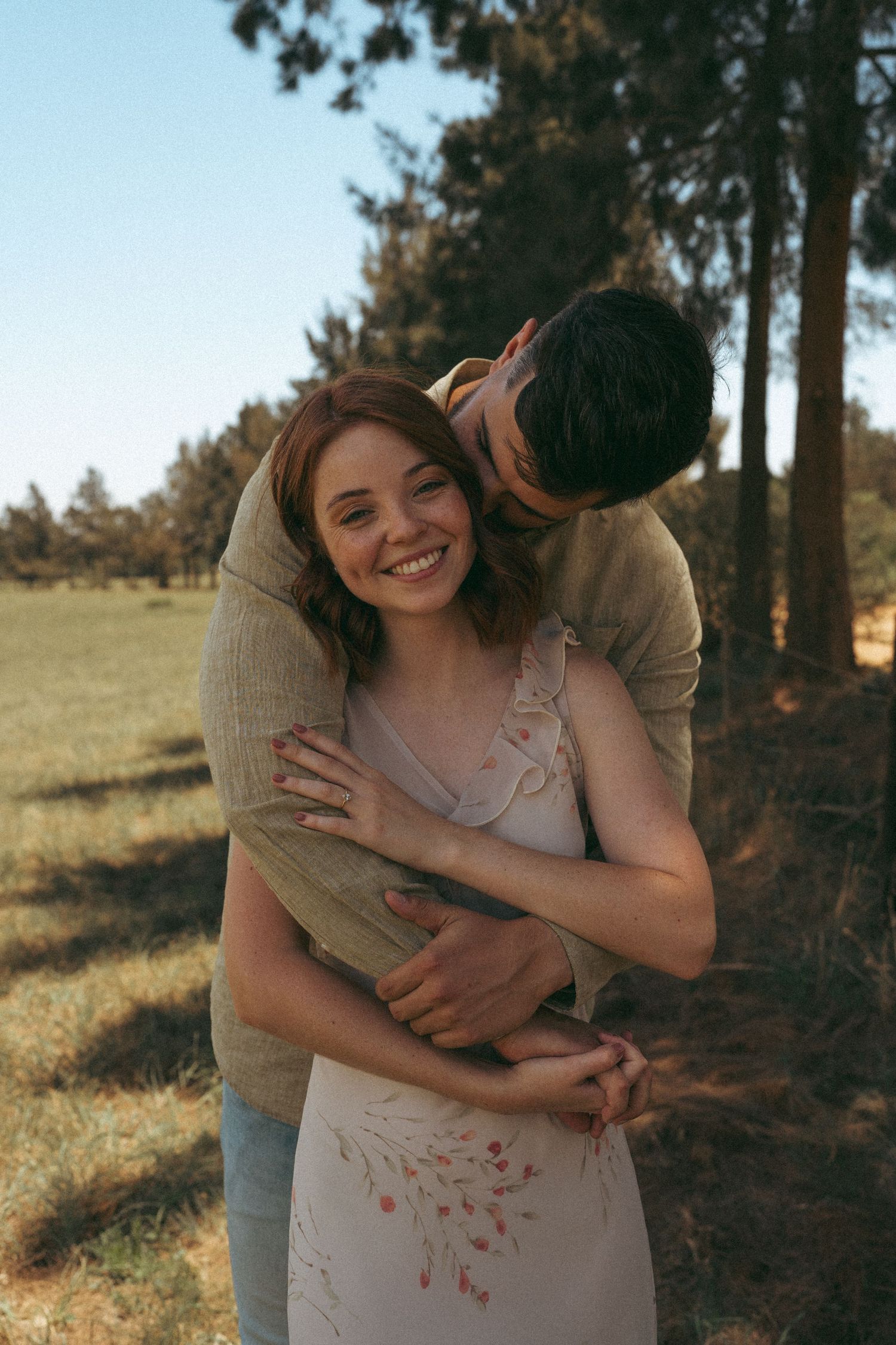 A couple shares joyful embraces in a sun-dappled forest setting.