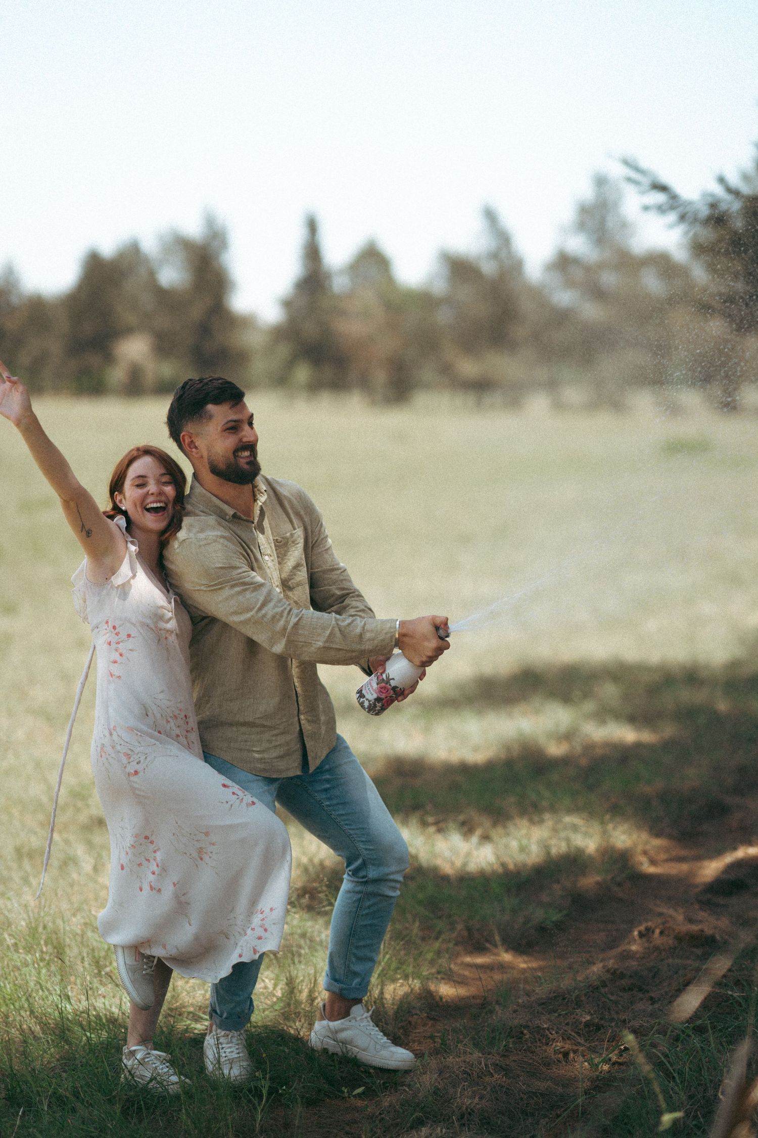 A couple plays and poses together in a grassy outdoor setting.
