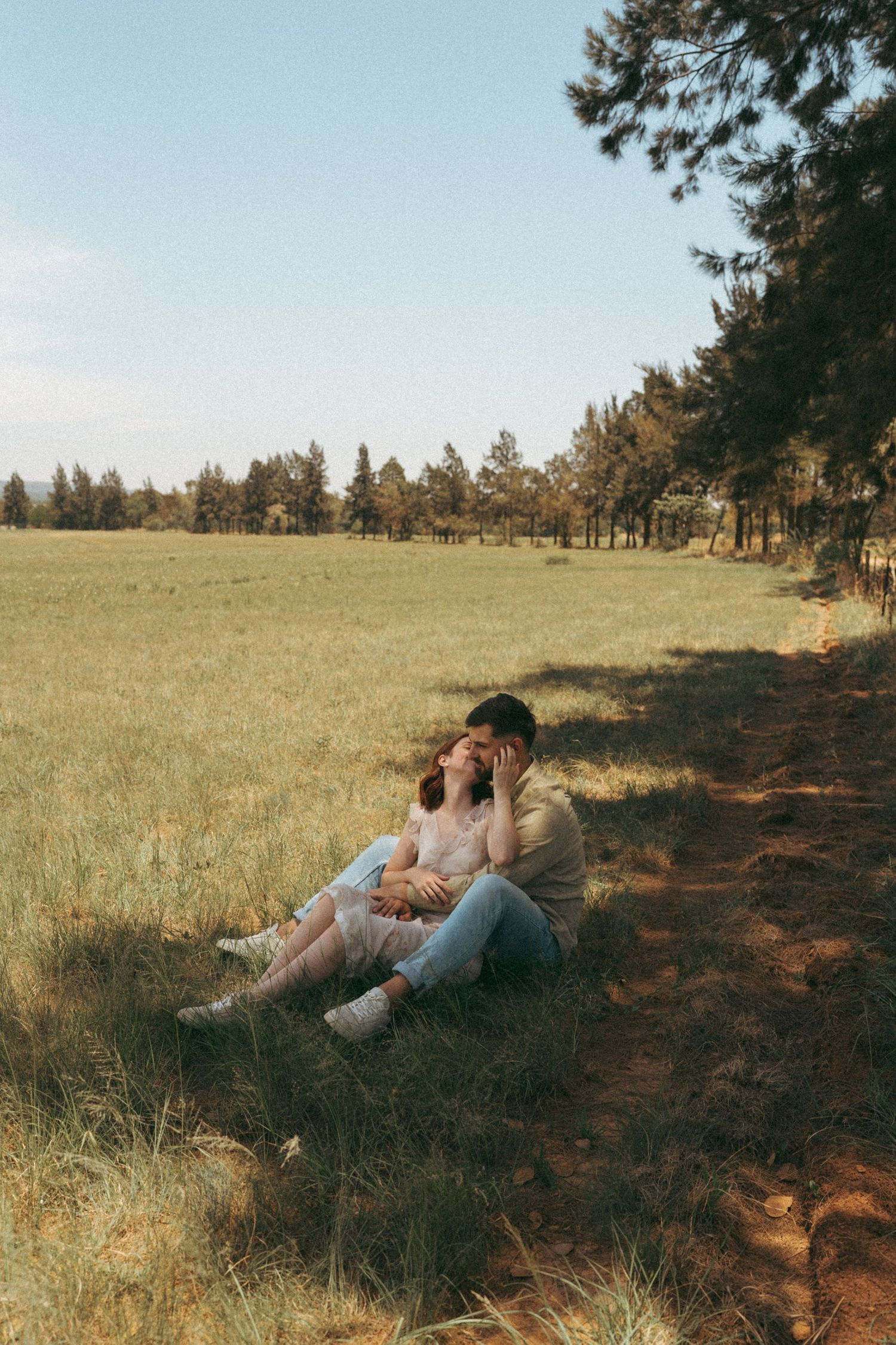 Romantic couple resting on hillside near pine forest during sunset.