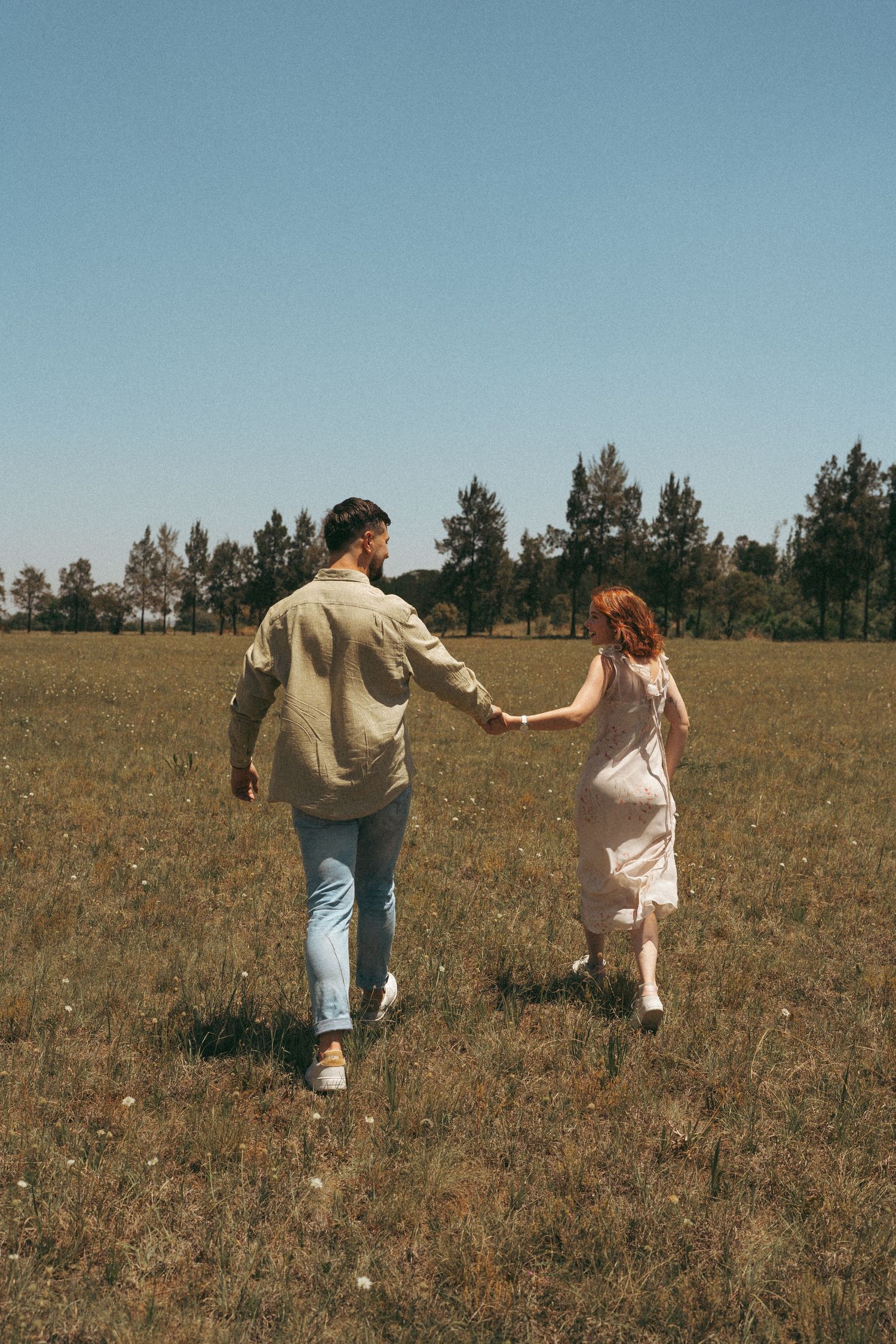 Couple dancing freely across a sunlit meadow with trees lining the horizon.