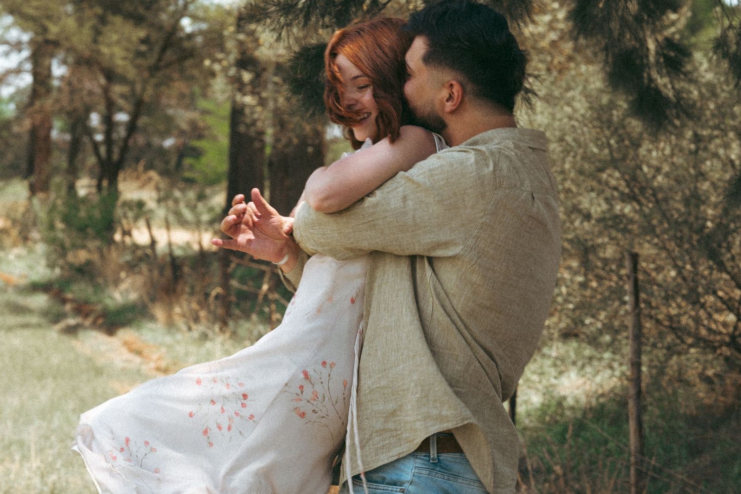 Couple sharing intimate moments on hillside with trees and golden light.