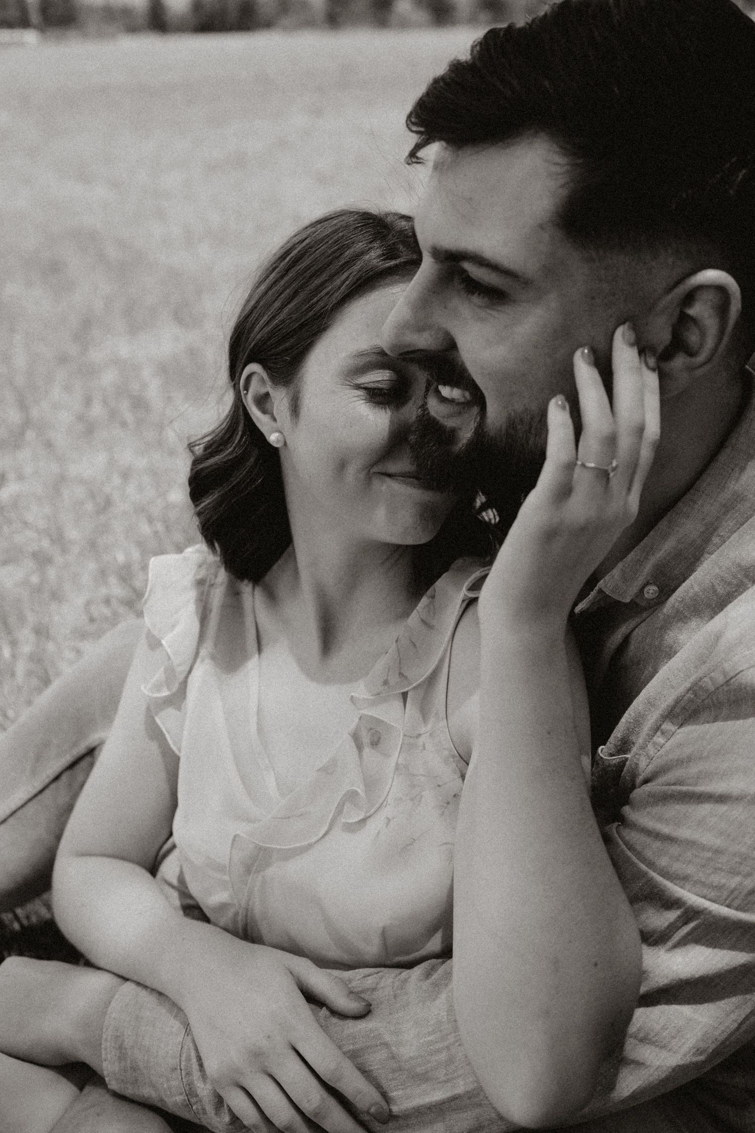 A black and white portrait of a couple embracing tenderly in a grassy field.