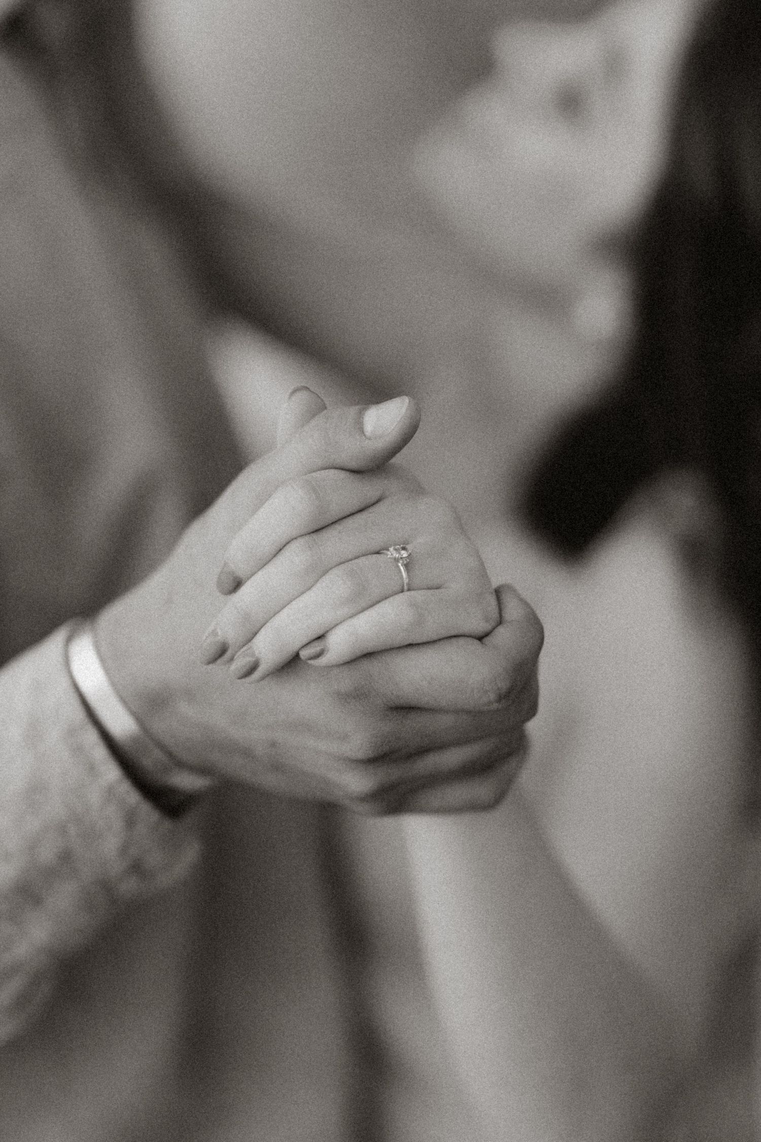 An intimate black and white photo of clasped hands with a wedding ring visible.