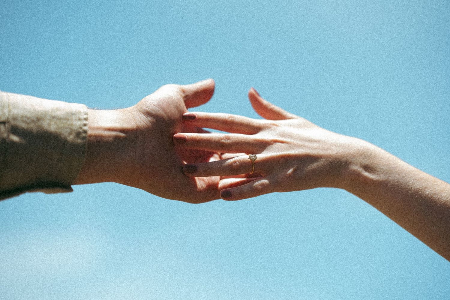 Two hands reaching towards each other against a bright blue sky.