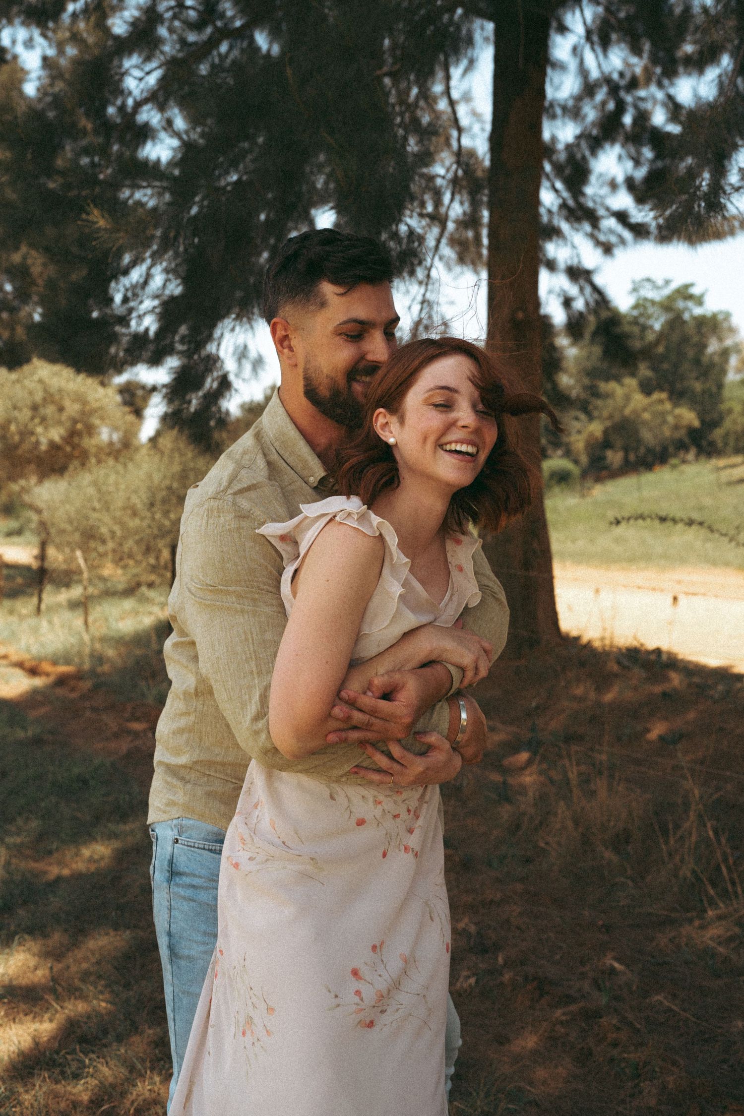 A romantic couple embrace under pine trees on a sunny afternoon.