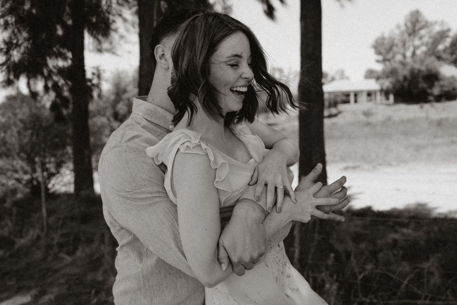 A candid black and white photo of a couple sharing a playful moment outdoors.