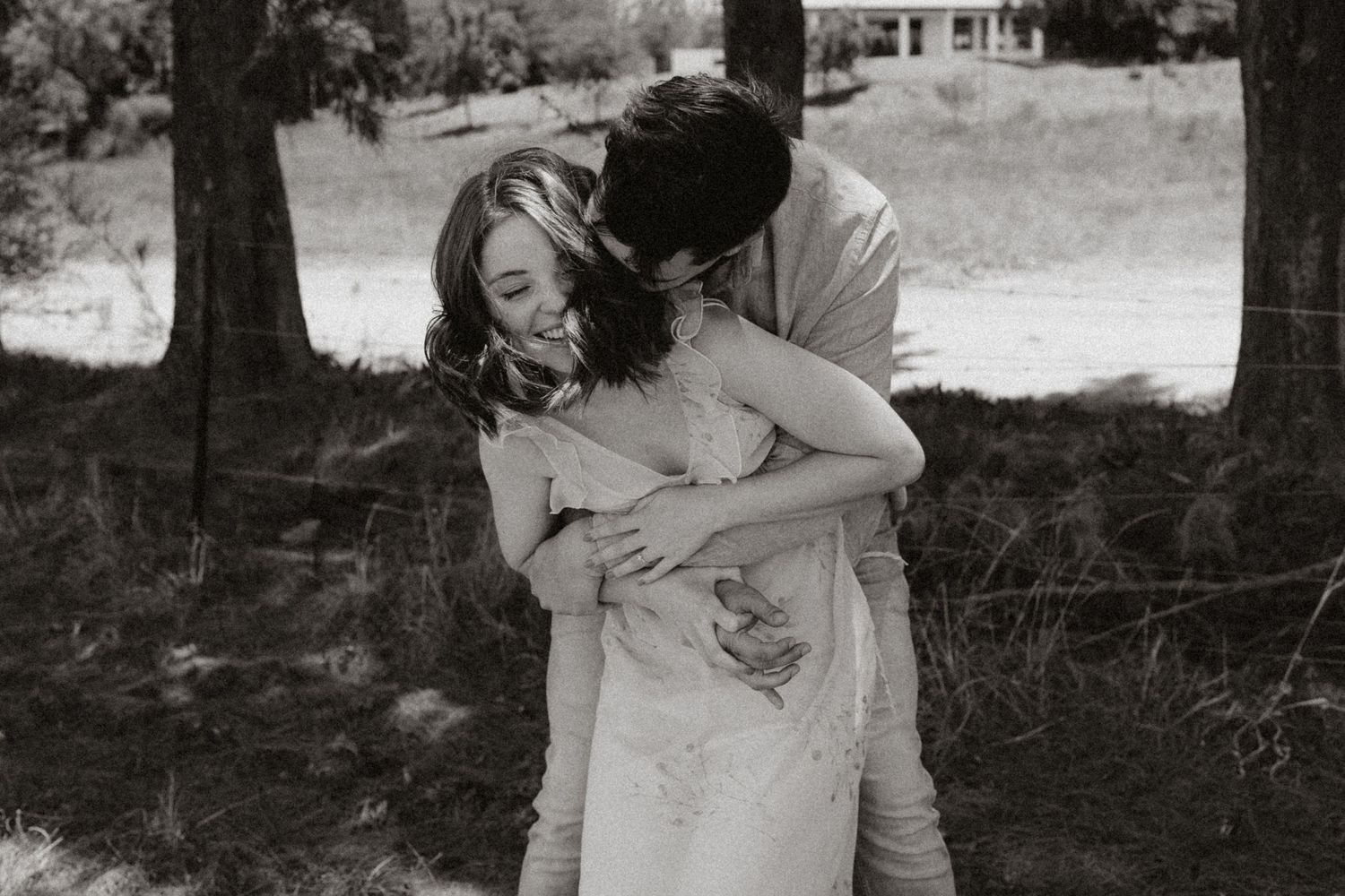 An intimate black and white portrait of a couple embracing under trees.