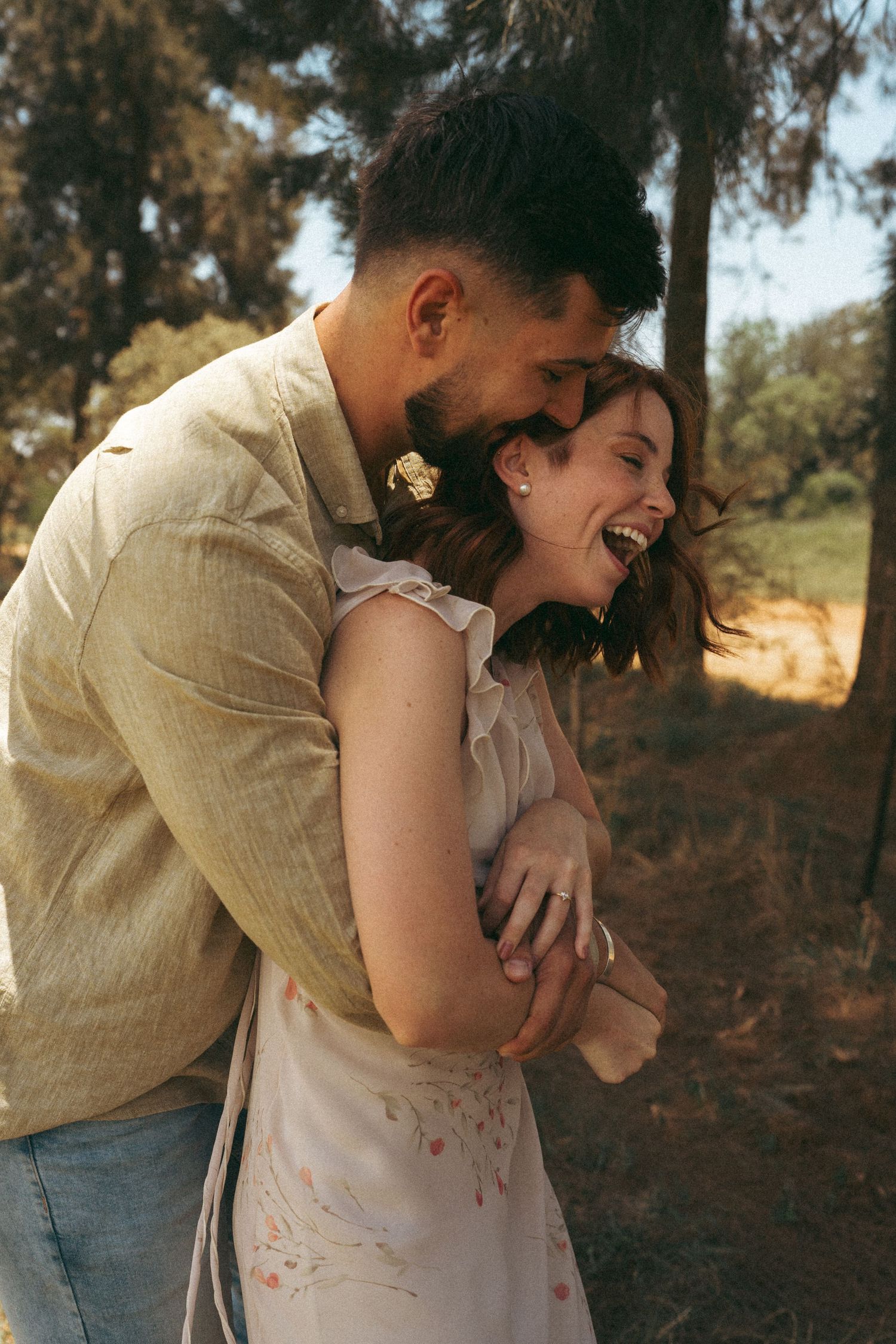 A tender moment between a couple laughing together in casual outdoor attire.