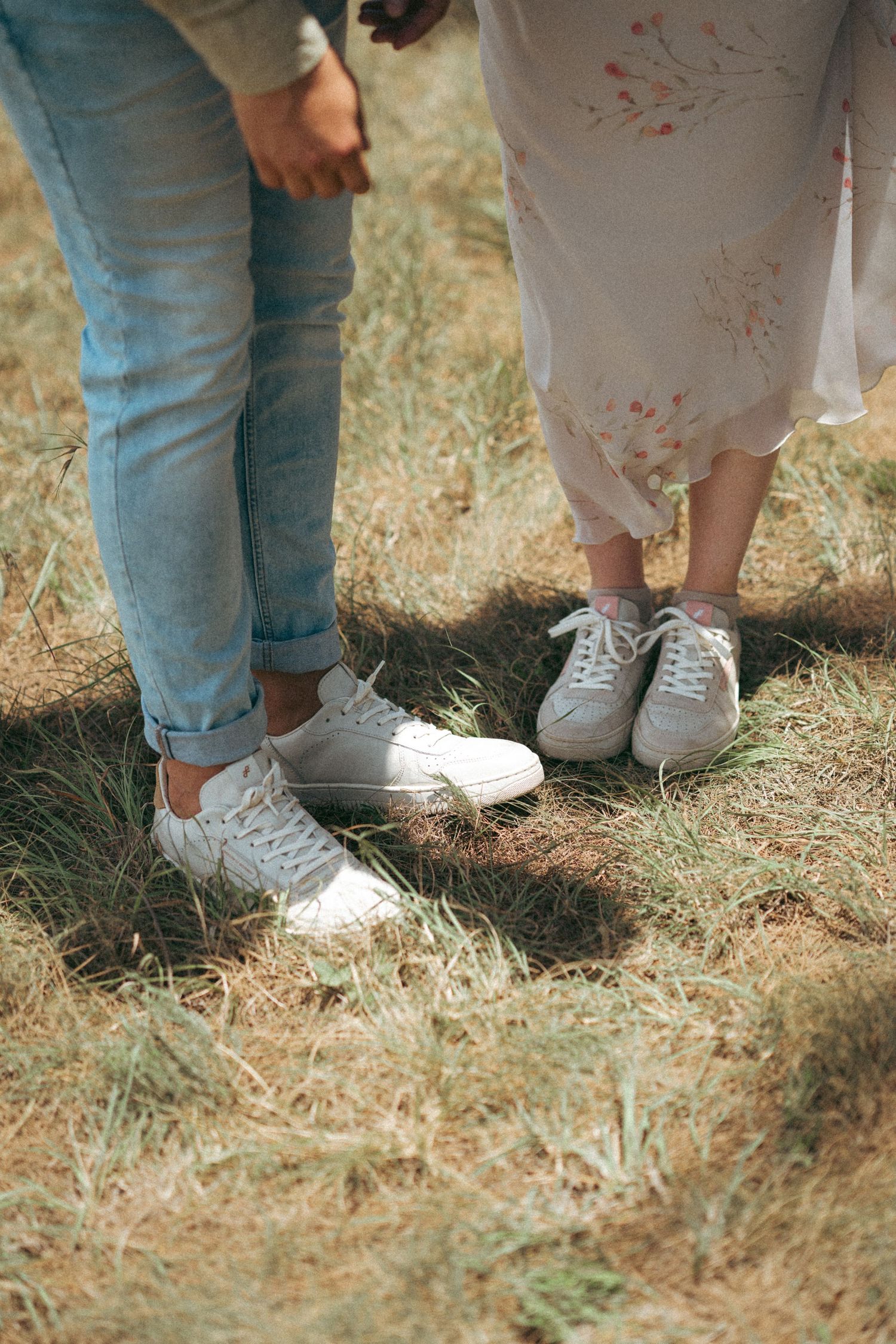 A close-up of two pairs of white sneakers standing together on grass.