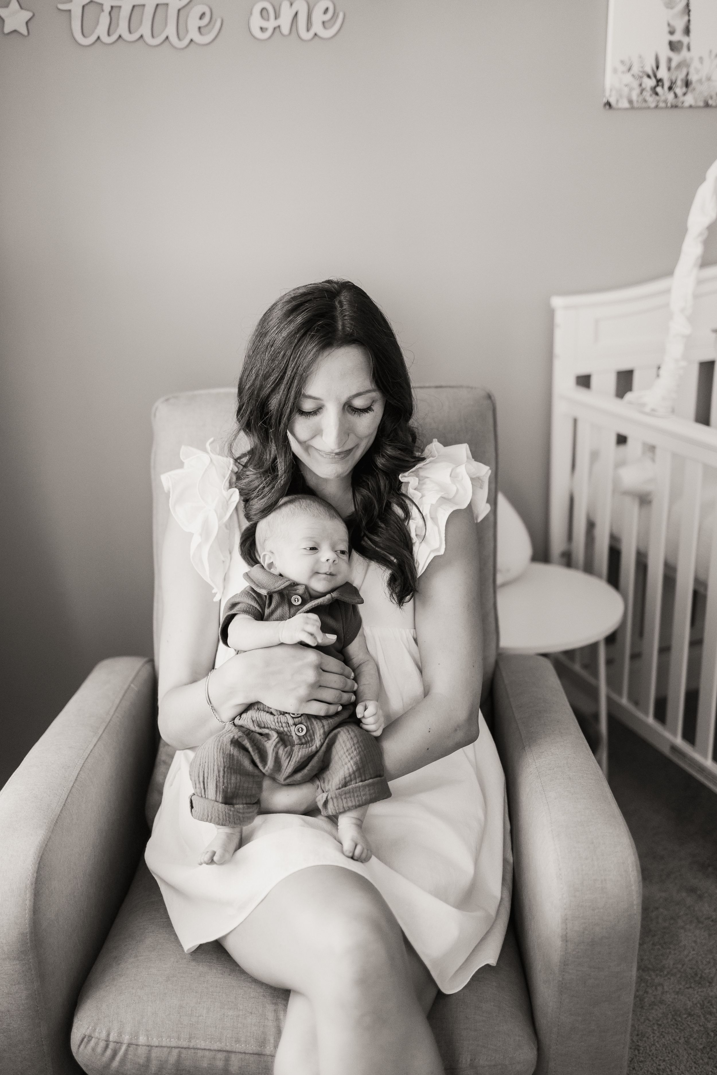 Black and white photo series showing tender moments between parent and baby in a cozy nursery armchair.
