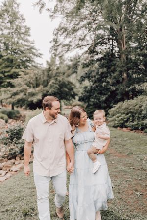 A family in light colored clothing walks together in a lush green outdoor setting.