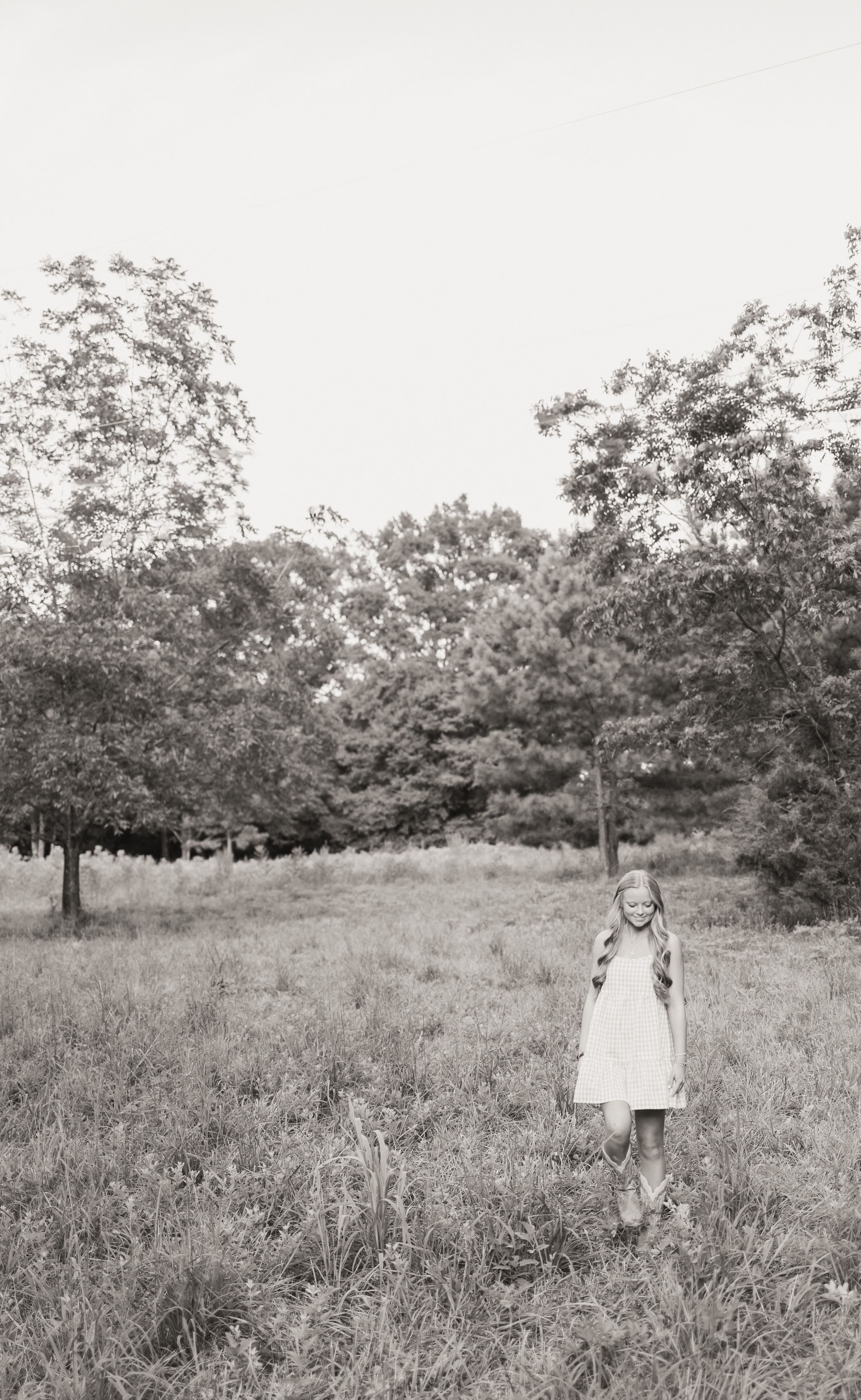 A small child in a white dress stands alone in a black and white field with scattered oak trees in the background.