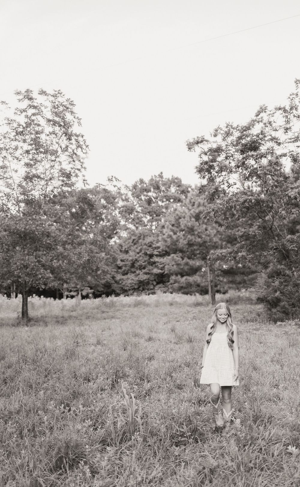 A small child in a white dress stands alone in a black and white field with scattered oak trees in the background.