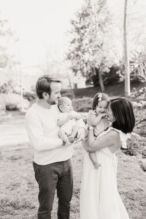 A black and white photo sequence shows a couple holding and interacting with a baby in an outdoor garden setting.