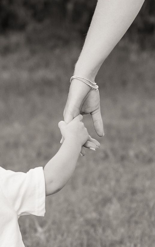 A black and white close-up of a child's hand holding an adult's finger.