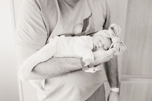A tender black and white photo showing a newborn baby being cradled in someone's arms.