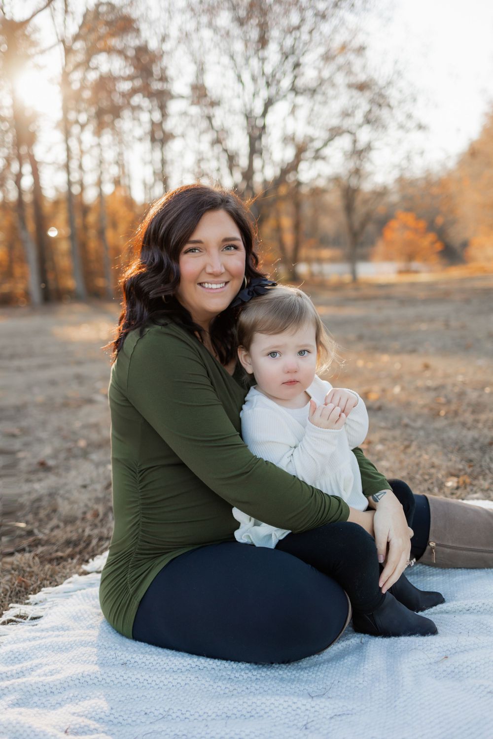 Mother and baby sit together on a blanket during an autumn outdoor photoshoot.