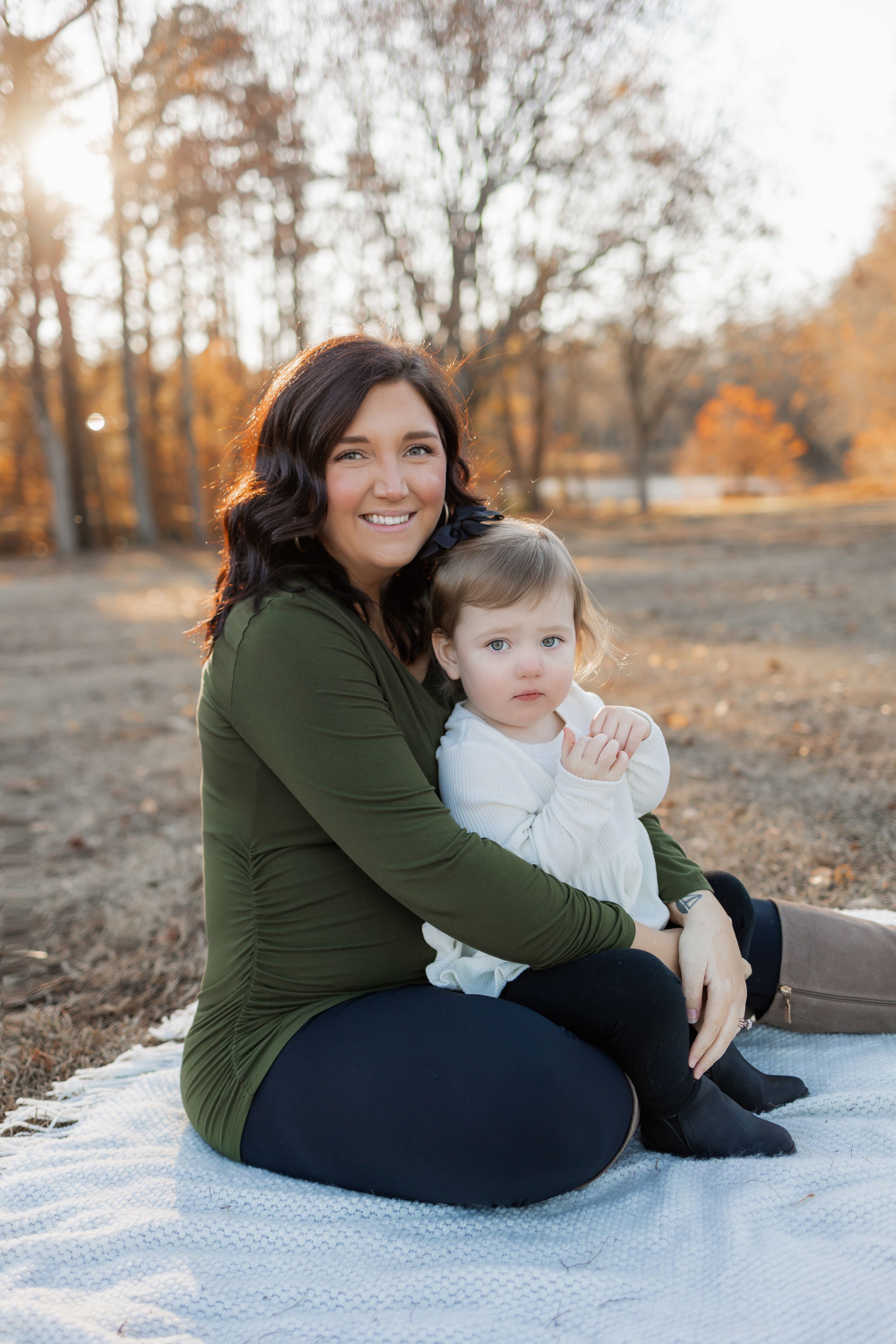 Mother and baby sit together on a blanket during an autumn outdoor photoshoot.