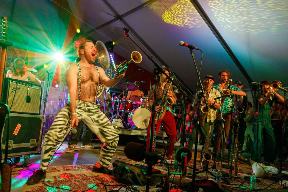 Energetic band performs under green lighting with brass section and colorful stage decorations.
