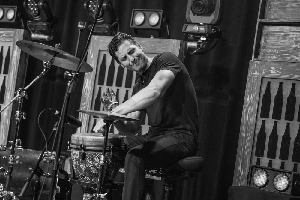 A musician performs energetically at a keyboard setup with wooden stage decorations in the background.