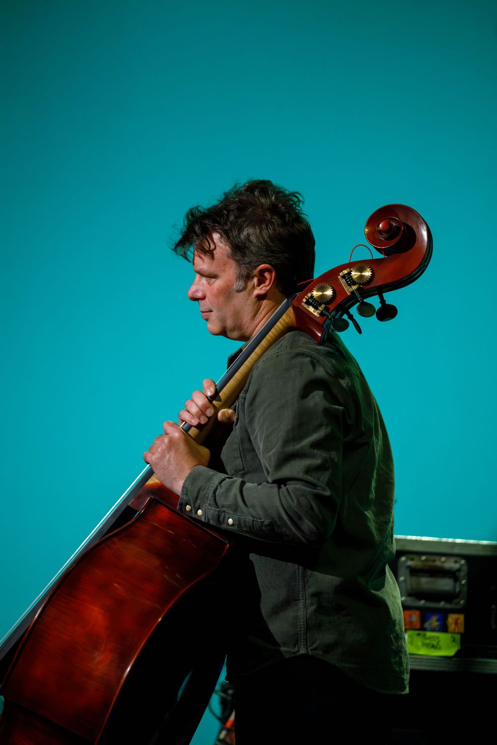 A musician plays an upright bass against a turquoise background during a performance.