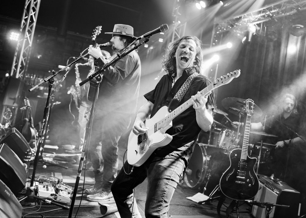 Rock band performs energetically on concert stage with dramatic lighting effects.