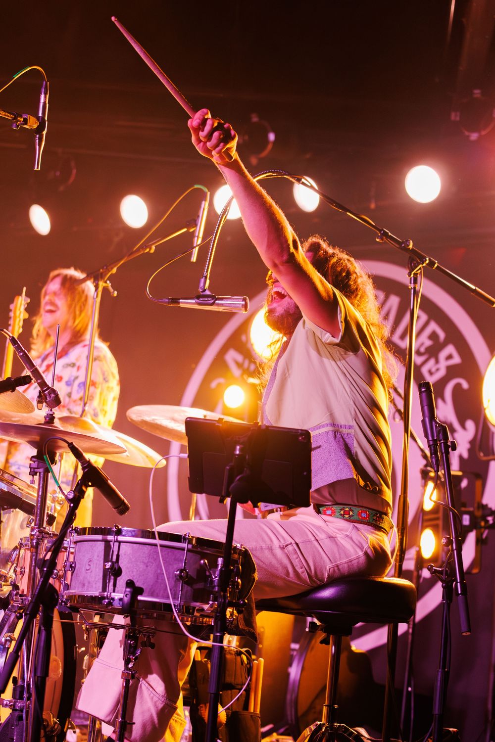 Musicians perform on stage with dramatic lighting and multiple microphone stands during a live concert performance.