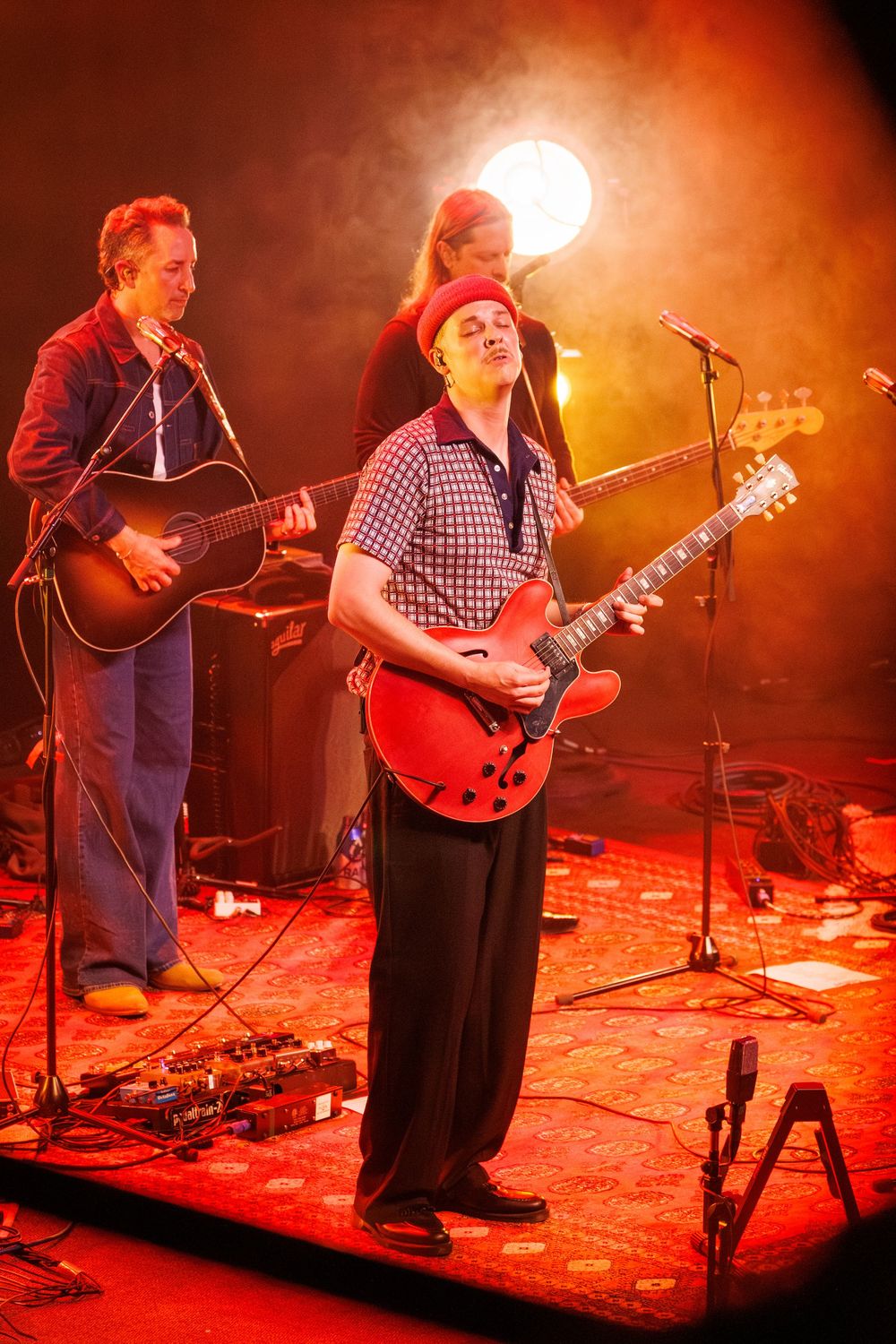 Musicians perform on stage bathed in dramatic red lighting during a live concert performance.