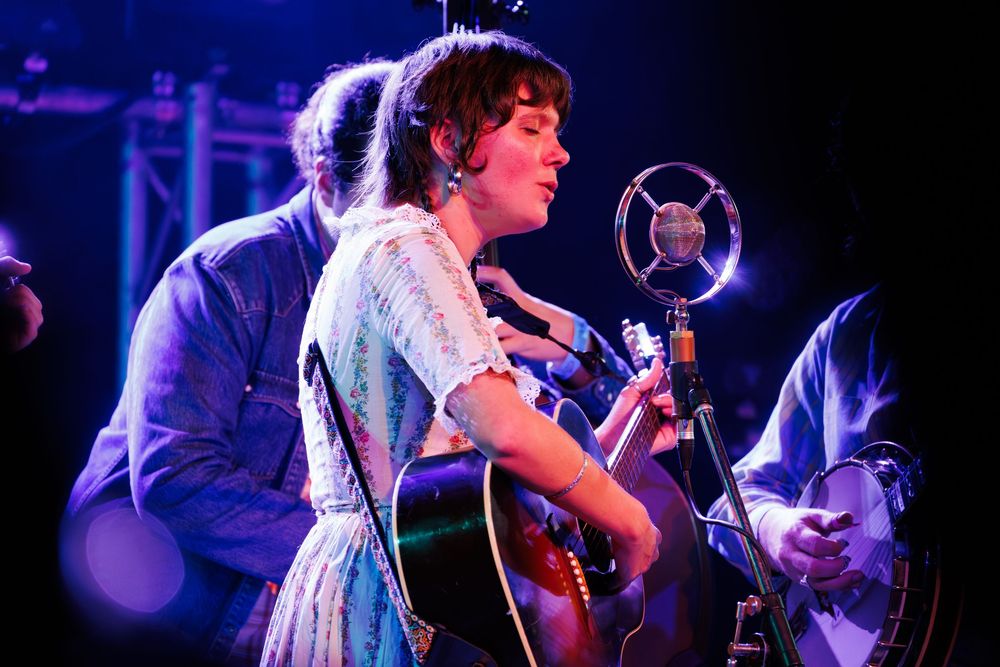 Musicians perform on stage during a live concert with dramatic blue lighting and energetic atmosphere.