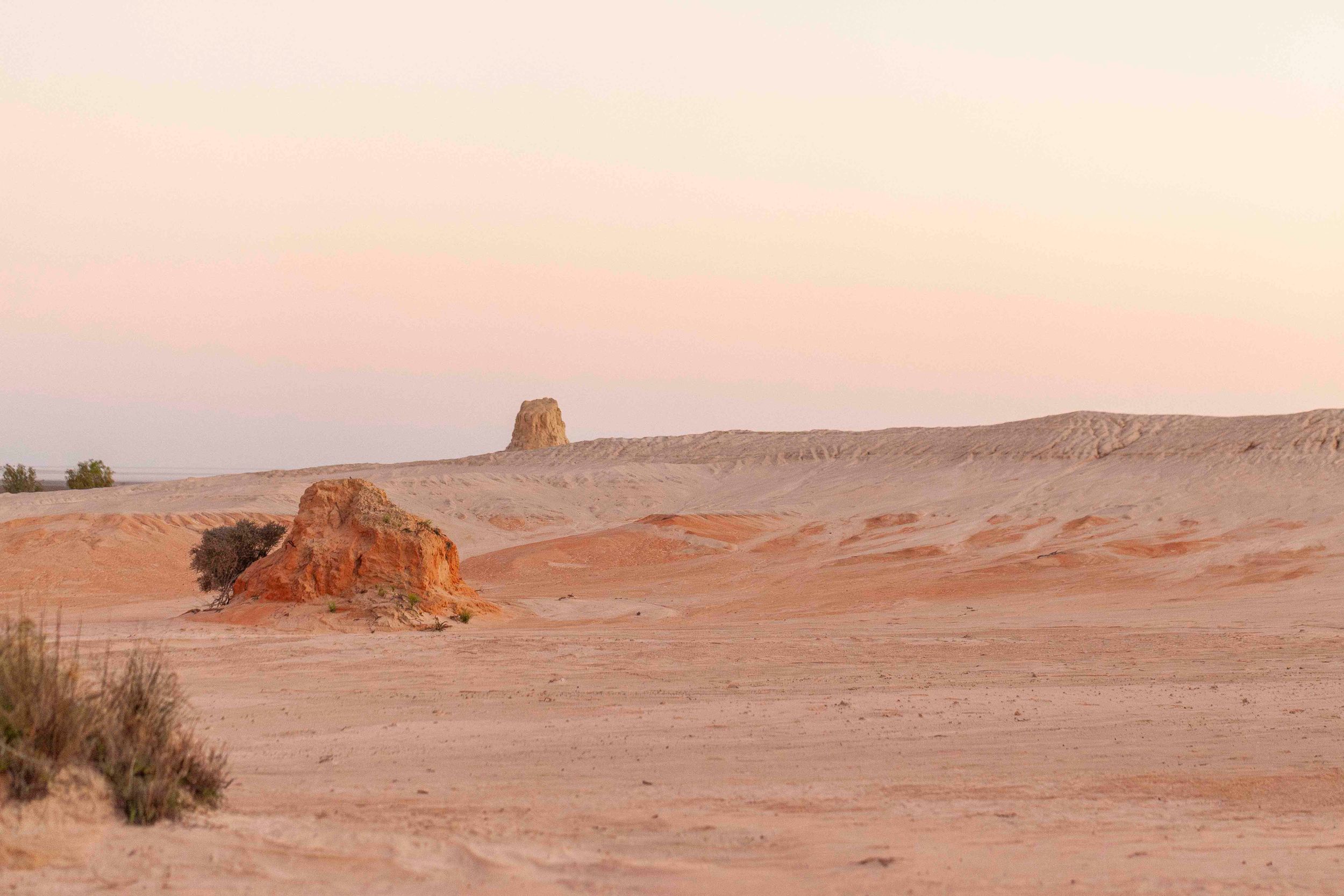 Sunset over red desert landscape with rock formations and sparse vegetation.