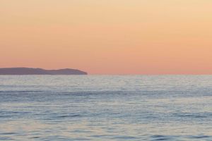 Peaceful ocean sunset with distant headland silhouetted against pink and orange sky.