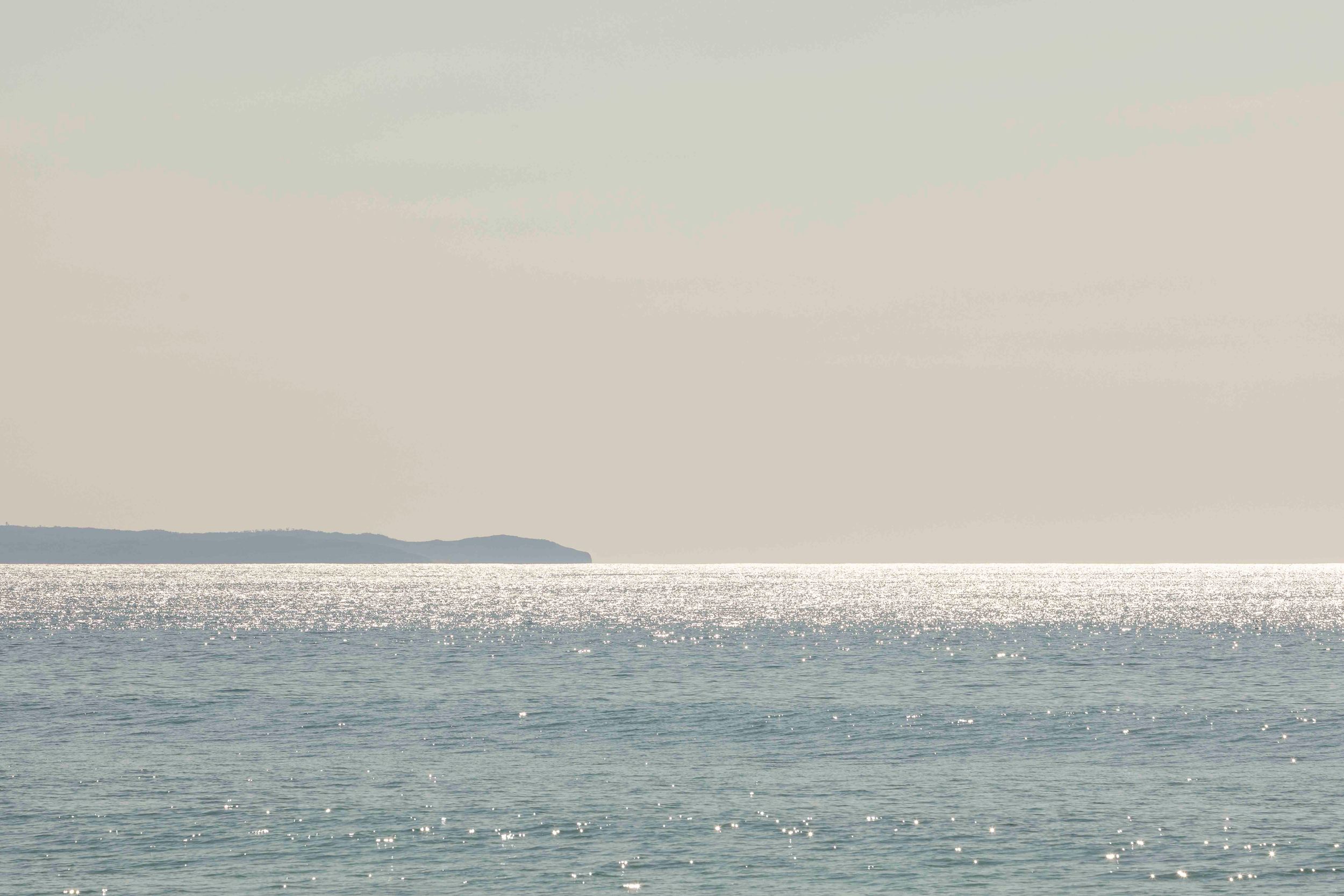 Serene seascape with shimmering water and distant coastline on the horizon.