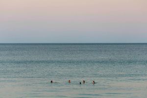 Swimmers dotting the calm ocean waters during sunset with pastel sky.
