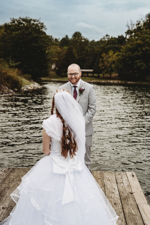 Bride and groom share a romantic moment on a wooden dock by a lake, with the bride in a white gown and veil.