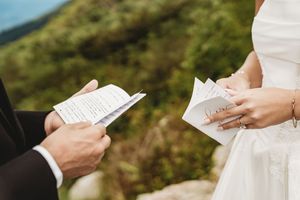 Couple exchanging handwritten wedding vows outdoors with lush green mountains in the background.