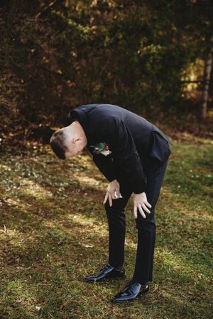 Person in dark suit bending over dramatically on grass outdoors.