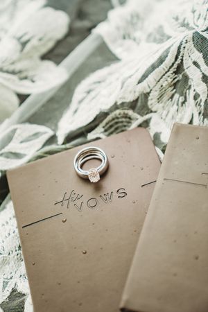 Wedding rings resting on kraft paper vow books with lace bridal veil backdrop.
