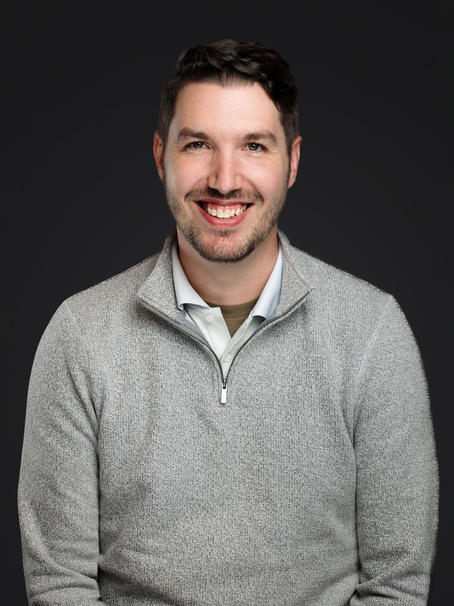 Professional headshot portrait of someone wearing a gray quarter-zip sweater against a dark background.