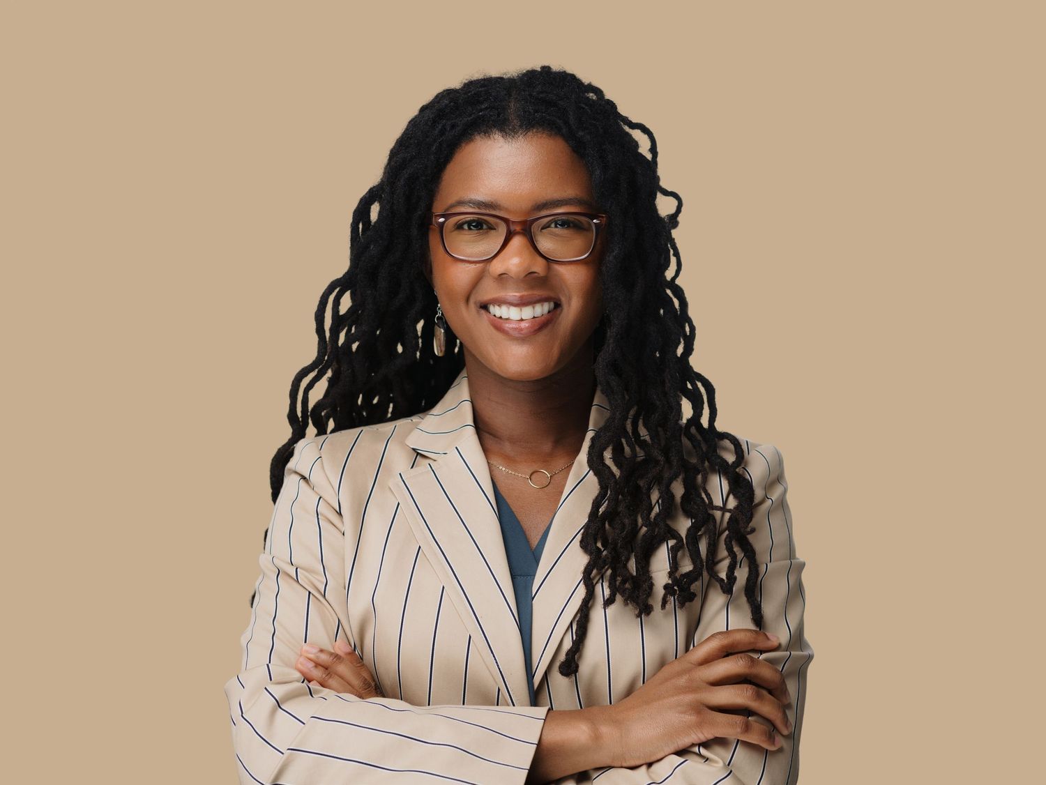 Professional Black woman in striped blazer with glasses, smiling confidently with arms crossed.