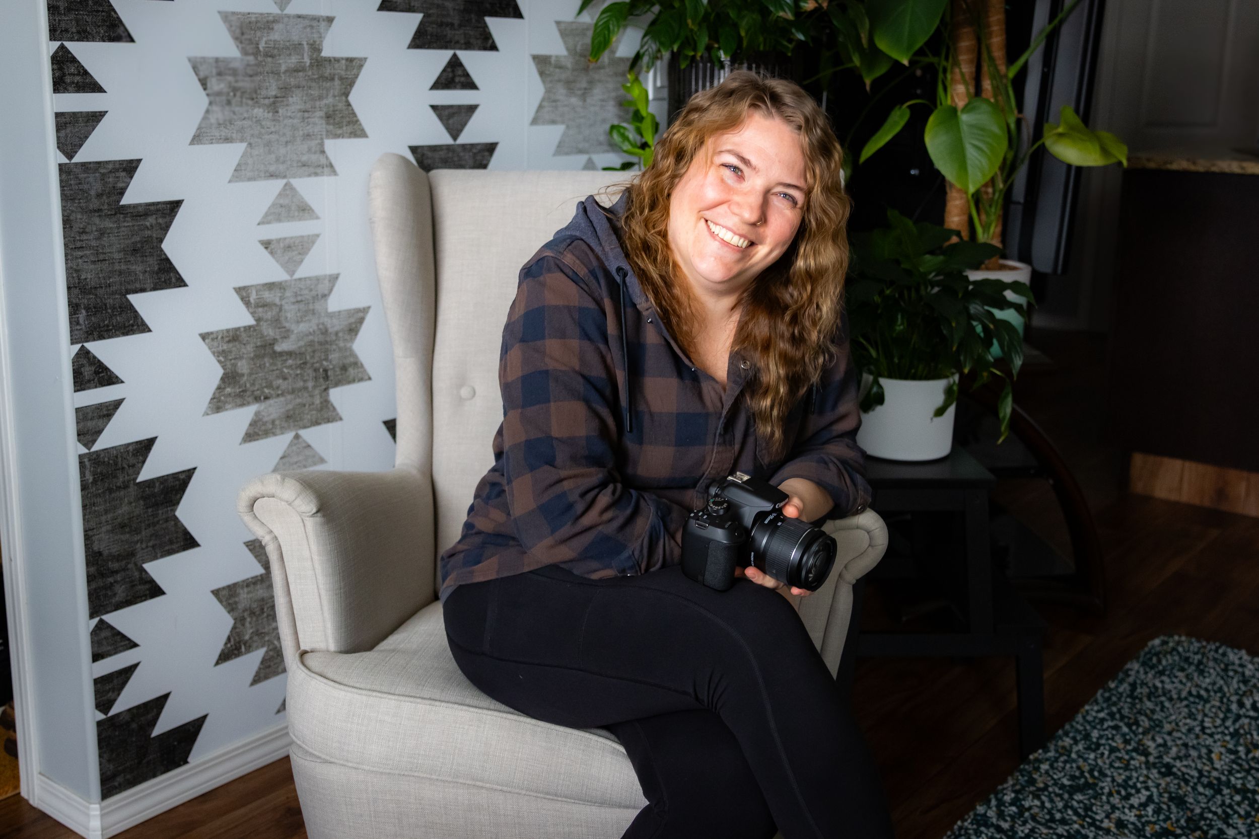 a women sitting in a chair, smiling with a camera in her hand.Family lifestyle session in Alberta by Creation Photography