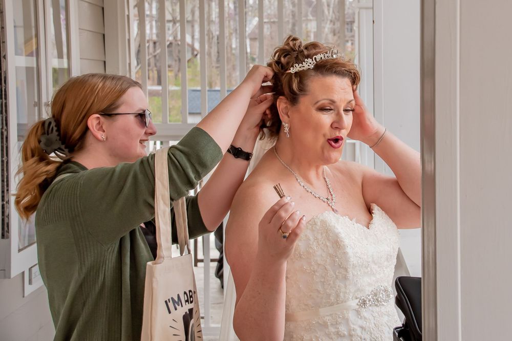 A person helps adjust a white lace wedding dress and hairpiece during bridal preparations.